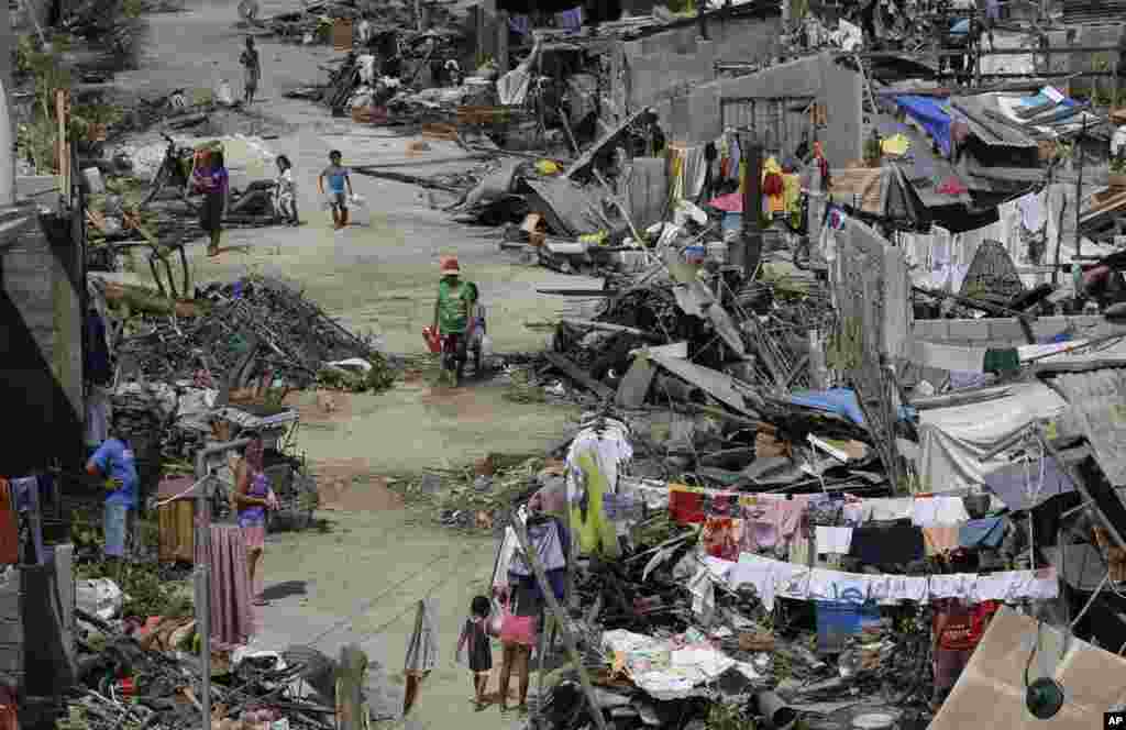 Para penyintas Topan Haiyan berjalan di antara reruntuhan rumah mereka di Maraboth, Filipina (14/11). (AP/Dita Alangkara)