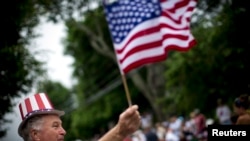 FILE - A man waves an American flag as he watches a July Fourth parade in the village of Barnstable, Massachusetts, July 4, 2014. 