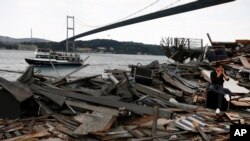 FILE - Backdropped by the Martyrs bridge over the Bosporus Strait, a man sits amongst the debris of the Reina nightclub that was attacked on New Year's Day, in Istanbul, May 22, 2017. Turkey's state-run news agency says authorities have partially destroyed the upscale Istanbul nightclub where an Islamic State group attacker killed 39 people. 