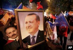 A supporter of the Justice and Development Party, (AKP), holds a portrait of Turkey's President Recep Tayyip Erdogan as people celebrate outside the AKP headquarters, in Istanbul, Turkey, late Sunday, Nov. 1, 2015.