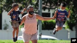 Seorang perempuan dan dua anak-anak mengenakan masker bermain di taman di tengah pandemi virus corona (COVID-19), di Los Angeles, California, 11 Juli 2020. (Foto: AP)