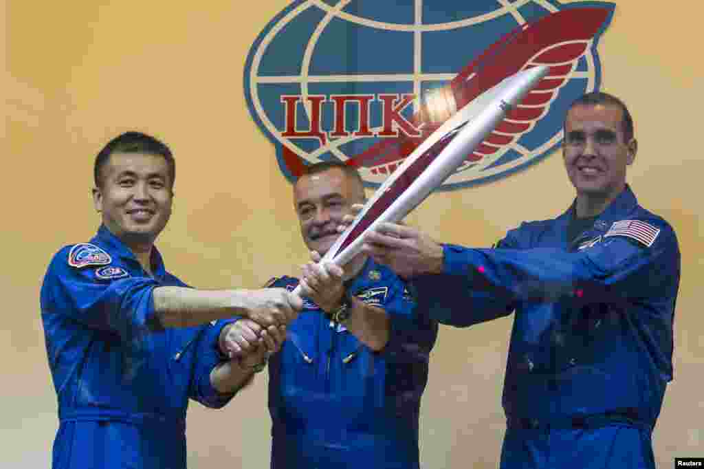 International Space Station crew members, Japanese astronaut Koichi Wakata, Russian cosmonaut Mikhail Tyurin and U.S. astronaut Rick Mastracchio, pose with the torch of the 2014 Sochi Winter Olympic Games after a news conference behind a glass wall at the