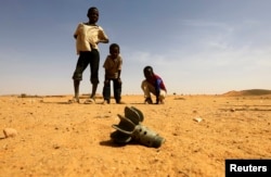 FILE - Children look at the fin of a mortar projectile that was found at the Al-Abassi camp for internally displaced persons, after an attack by rebels, in Mellit town, North Darfur, March 25, 2014.