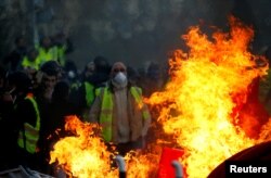 FILE - Protesters wearing yellow vests are seen behind a fire as they attend a demonstration of the "yellow vests" movement in Angers, France, Jan. 19, 2019.
