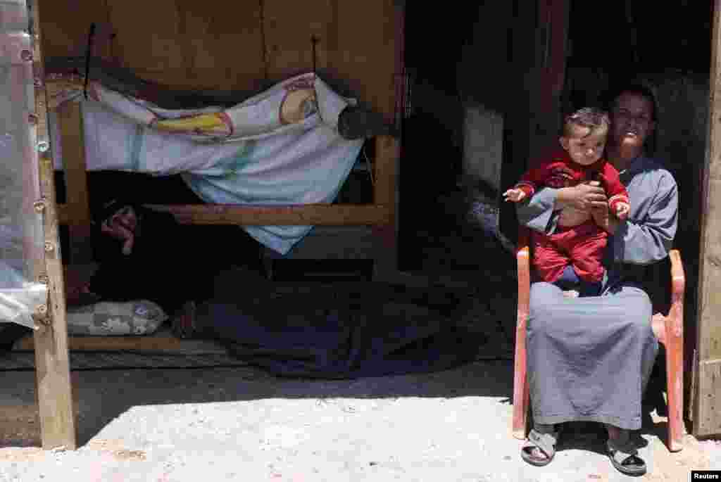 Syrian refugees sit outside their home in a refugee camp in the eastern Lebanese town of Anjar near the Syrian border, May 13, 2014.