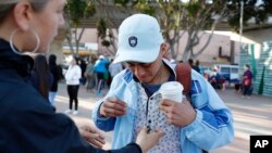 FILE - A man who only gave his first name as Ariel, of Honduras, receives an image of Saint Jude from a woman before crossing into the United States to begin his asylum case after being returned to Mexico, March 19, 2019, in Tijuana, Mexico.