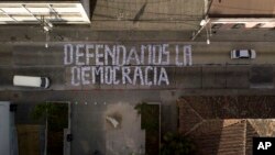 Seen from above, a sign covering a street forms the Spanish phrase: "We defend democracy," made with photographs of the president and his cabinet, outside the Constitutional Court in Guatemala City, Jan. 9, 2019. 