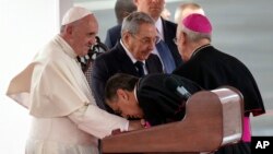 A member of Cuba's church leadership kisses the hand of Pope Francis as Cuban President Raul Castro stands alongside during the pope's arrival ceremony at the airport in Havana, Sept. 19, 2015.