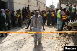 FILE - An injured man walks away as rescue workers search after a blast near the home of the home minister of Punjab province, Shuja Khanzada, in Attock, Pakistan, Aug. 16, 2015.