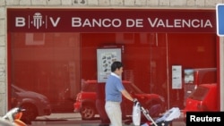 A man pushes a pram past a Banco de Valencia bank branch in Madrid, June 25, 2012. 