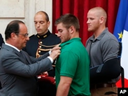 French President Francois Hollande, left, awards with the Legion of Honor Alek Skarlatos a U.S. National Guardsman from Roseburg, Oregon, while U.S. Airman Spencer Stone, right, looks on at the Elysee Palace, Monday Aug.24, 2015 in Paris, France.