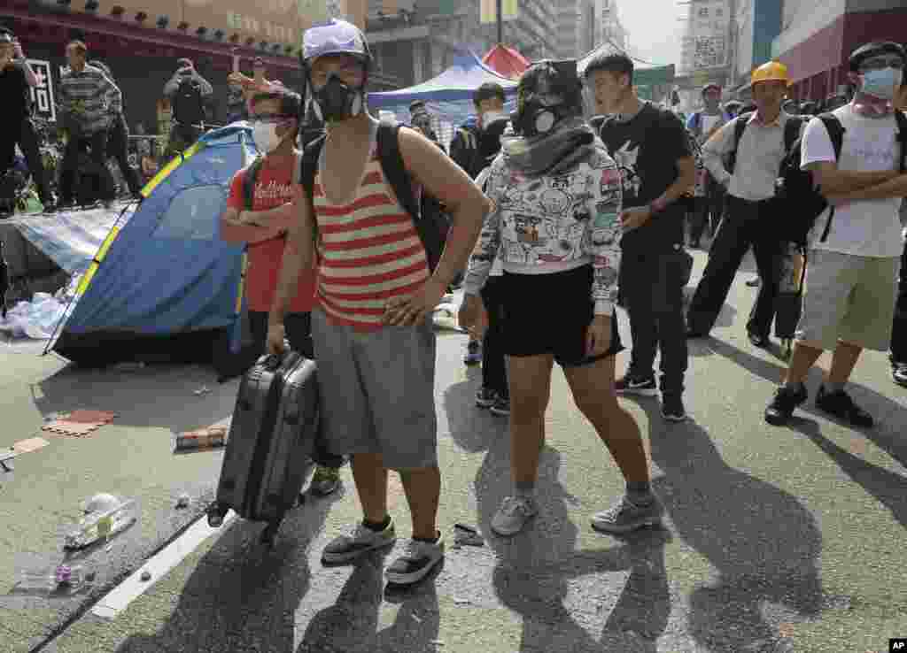 Para demonstran yang mengenakan masker membawa barang-barang milik mereka sementara ribuan polisi membersihkan barisan barikade besi. Polisi lainnya membongkar tenda dan kanopi dan menyingkirkan rintangan-rintangan lainnya di lokasi yang diduduki di distrik Mong Kok, Hong Kong, 26 November 2014.