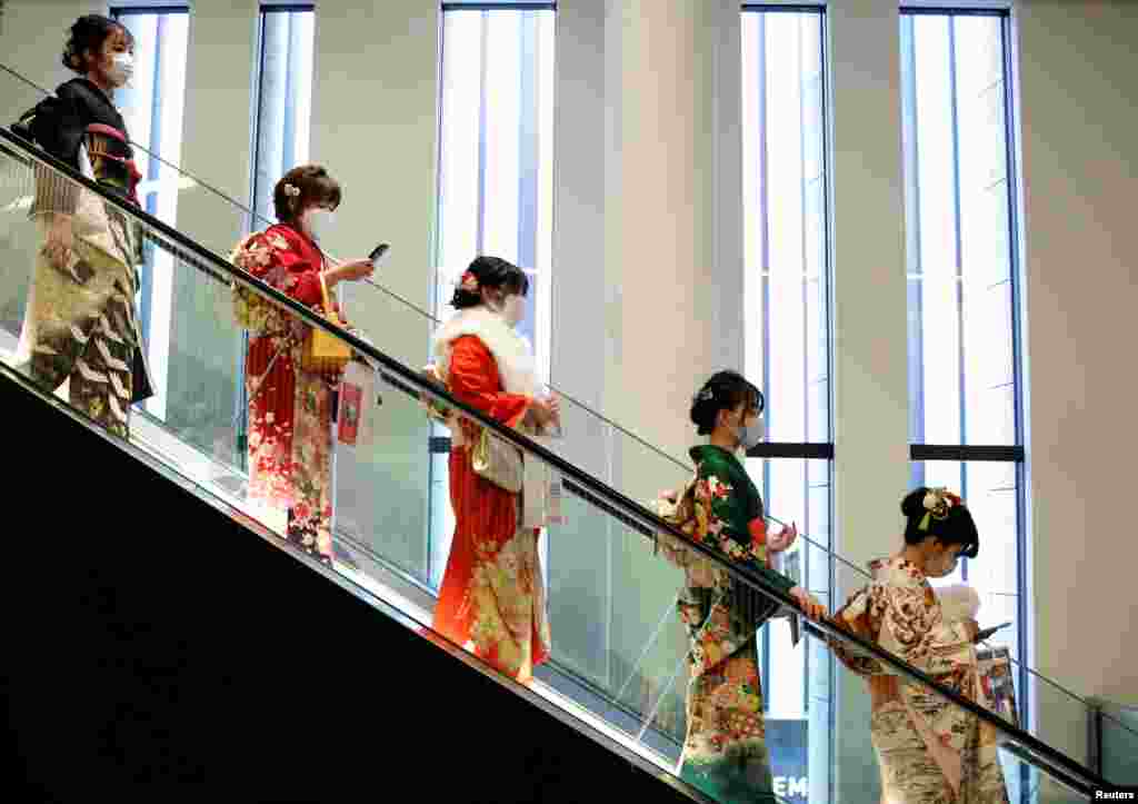 Women wearing kimono and protective masks ride on an escalator at Coming of Age Day celebration ceremony venue in Tokyo, Japan.