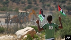 A Palestinian boy holds Palestinian flags as an Israeli tractor removes parts of Israel's separation barrier between the West Bank village of Bilin, near Ramallah, and the Jewish settlement of Modiin Illit, June 26, 2011