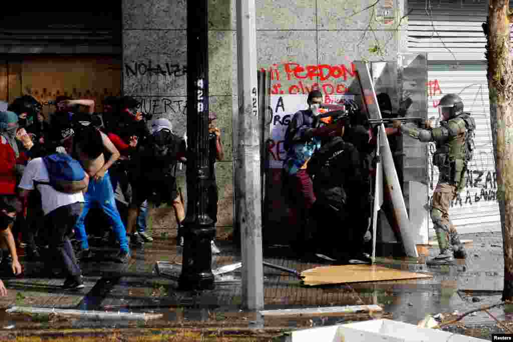 A police officer points his gun at demonstrators during a protest against Chile&#39;s state economic model in Santiago, Oct. 22, 2019.