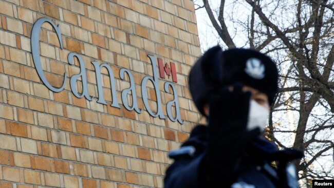在加拿大驻北京大使馆外一名中国警察向摄影记者打手势。（2018年12月12日）