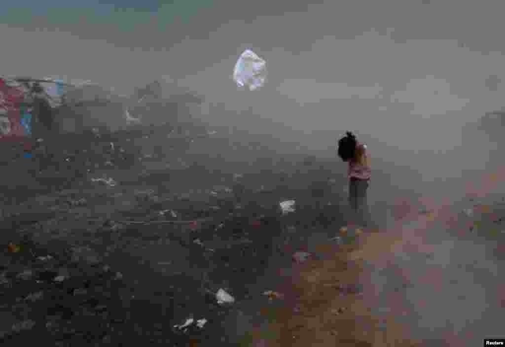 A girl protects herself from garbage and dust, blown by a gust of wind, in a slum in Islamabad, Pakistan.