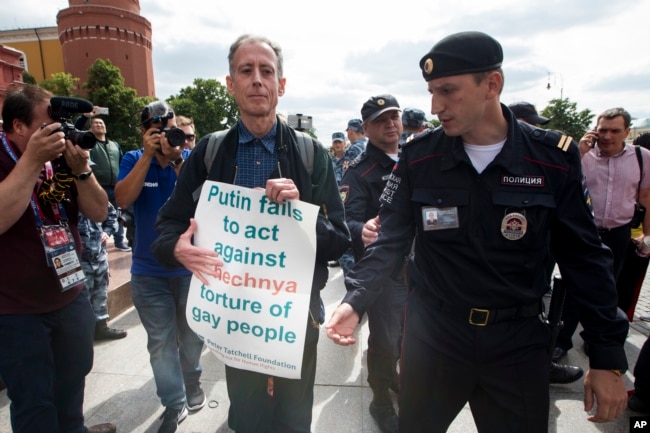 FILE - Russian police detain gay rights activist Peter Tatchell, center, as he holds a banner that reads "Putin fails to act against Chechnya torture of gay people" near Red Square in Moscow, Russia, June 14, 2018.