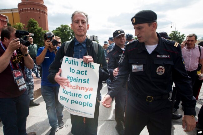 FILE - Russian police detain gay rights activist Peter Tatchell, center, as he holds a banner that reads "Putin fails to act against Chechnya torture of gay people" near Red Square in Moscow, Russia, June 14, 2018.