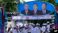 Supporters of Prime Minister Hun Sen's Cambodian People's Party dance under portraits of the party leaders, from left, Chea Sim, Hun Sen and Heng Samrin, during an election campaign in Phnom Penh, Cambodia, Thursday, June 27, 2013.