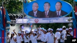 Supporters of Prime Minister Hun Sen's Cambodian People's Party dance under portraits of the party leaders, from left, Chea Sim, Hun Sen and Heng Samrin, during an election campaign in Phnom Penh, Cambodia, Thursday, June 27, 2013. 