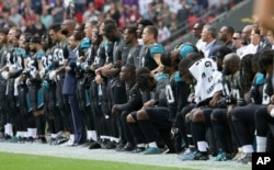 Jacksonville Jaguars players lock arms and kneel down during the playing of the U.S. national anthem before an NFL football game against the Baltimore Ravens at Wembley Stadium in London, Sept. 24, 2017.