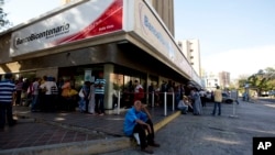 FILE - Customers wait outside of a government bank to get new bank notes in Maracaibo, Venezuela, Aug. 21, 2018. 