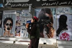 A Taliban fighter walks past a beauty salon with images of women defaced using spray paint in Shar-e-Naw in Kabul on August 18, 2021.