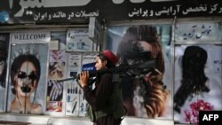 Seorang pejuang Taliban berjalan melewati salon kecantikan dengan gambar perempuan dirusak menggunakan cat semprot di Shar-e-Naw di Kabul pada 18 Agustus 2021. (Foto: AFP/Wakil Kohsar)
