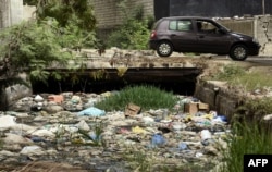 FILE - A car passes by a canal full with trash in Dakar, June 2, 2018.
