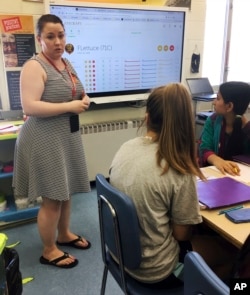 In this May 23, 2018 photo, teacher Gianna Gurga, left, speaks to students Faith Broadway, center, and Maisha Chowdhury Jabia, right, as she leads a class on financial literacy at Dag Hammarskjold Middle School in Wallingford, Conn. (AP Photo/Michael Meli