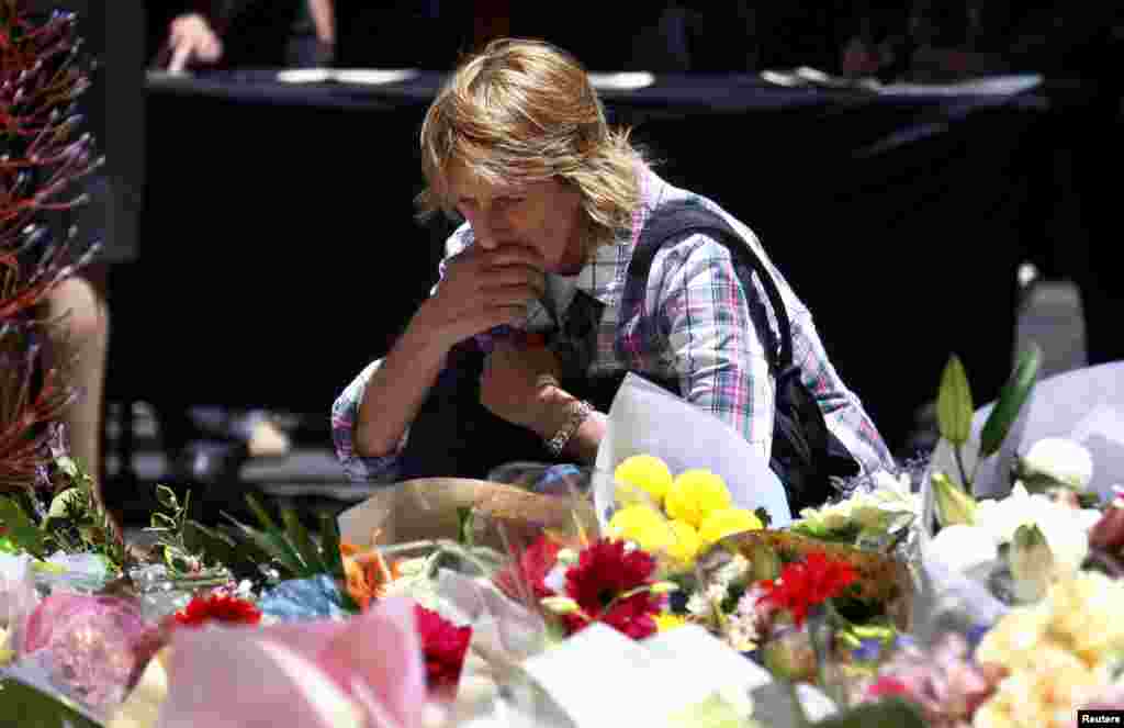 A woman reacts after placing a floral tribute amongst thousands of others that have been placed near the cafe where hostages were held for over 16 hours, in central Sydney, December 16, 2014.