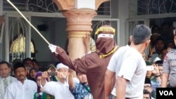 Algojo pelaksana cambuk mengayunkan rotan ke punggung pelanggar syariah di Banda Aceh, 19 September 2014 (Foto: VOA/Budi Nahaba)