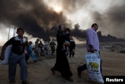 Civilians return to their village after it was liberated from Islamic State militants, south of Mosul in Qayyara, Iraq, Oct. 22, 2016. The fumes in the background are from oil wells that were set ablaze by Islamic State militants.