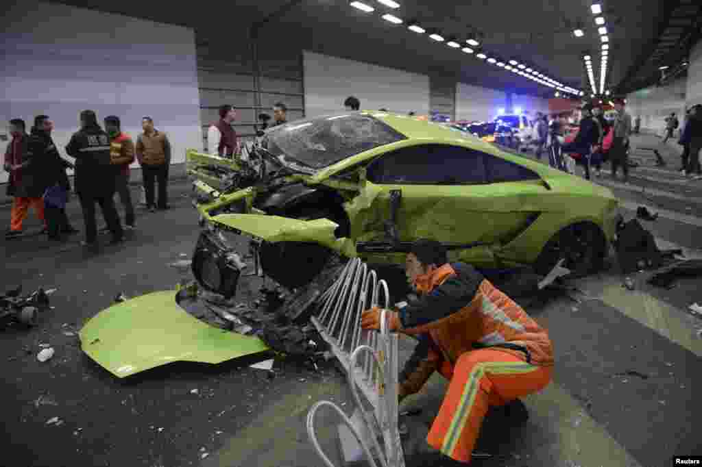 Seorang petugas mencoba memindahkan bagian pagar yang rusak di bawah mobil Lamborghini yang rusak setelah bertabrakan dengan sebuah mobil Ferrari di dalam terowongan di in Beijing, China, 12 April 2015. Satu penumpang terluka dalam kecelakaan tersebut dan polisi sedang mencari tahu penyebabnya. Warga yang tinggal di dekat area itu mengatakan terowongan itu biasa digunakan untuk balapan mobil liar di Beijing, seperti yang dilaporkan media setempat.