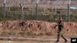 FILE - A Turkish soldier walks by the border fence with Syria.