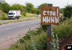 FILE - A poster reading 'Stop! Mines!' stands at a verge near the city of Kramatorsk, Donetsk region, eastern Ukraine, June 24, 2014.