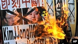 South Korean protesters burn a placard showing the defaced portraits of North Korean leader Kim Jong-il (L) and his youngest son and successor-in-waiting Kim Jong-un (R) during an anti-North Korea rally in Seoul, 28 Dec 2010