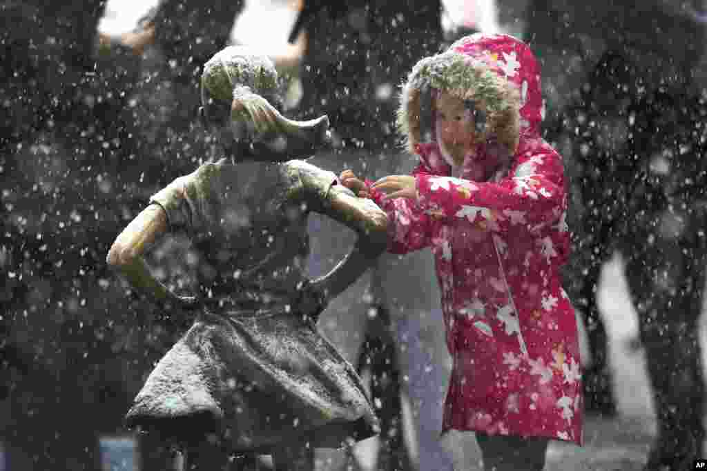 A young girl brushes off snow on the Fearless Girl statue in lower Manhattan on Nov. 15, 2018, in New York, as one of the first big storms of the season moved across the eastern half of the country Thursday.