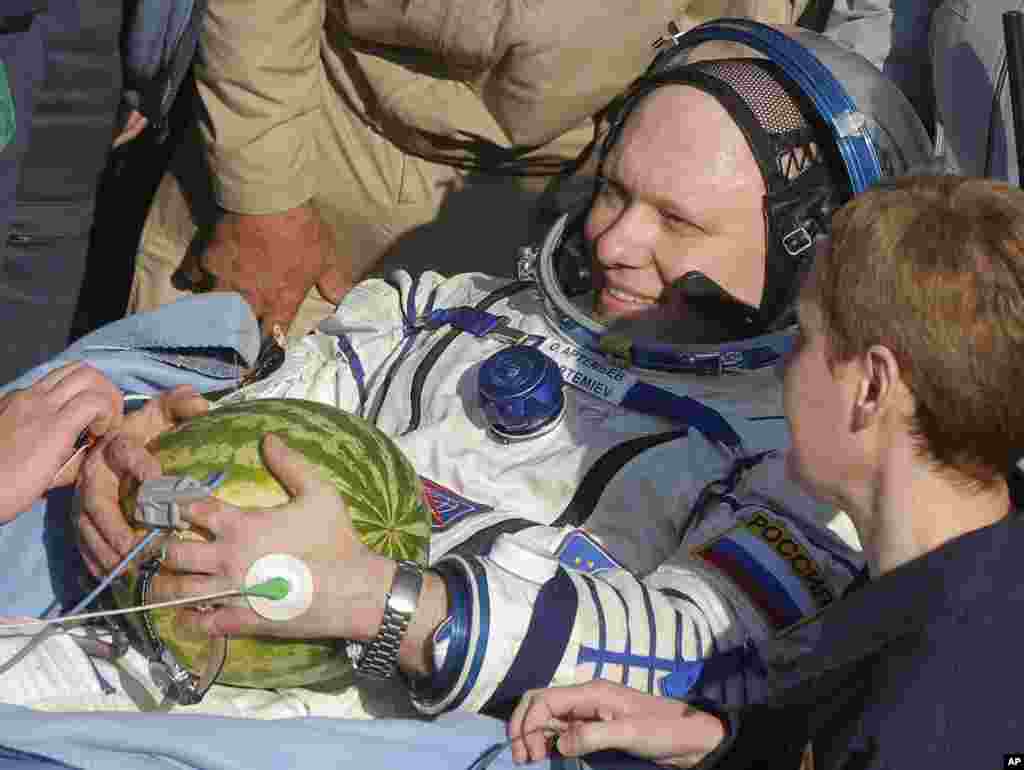 Russian cosmonauts Oleg Artemiev holds a watermelon while being examined by medics of a rescue team after landing, Sept. 11, 2014.