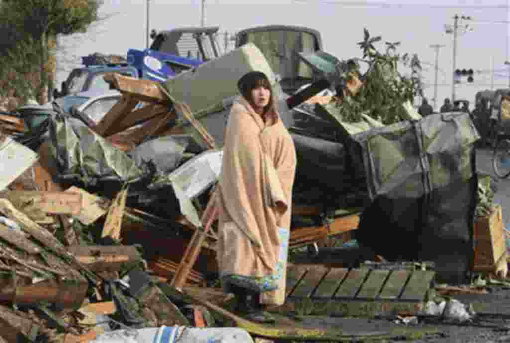 Una mujer se cubre con una manta ante los restos destruidos de una de las ciudades afectadas en Japón.