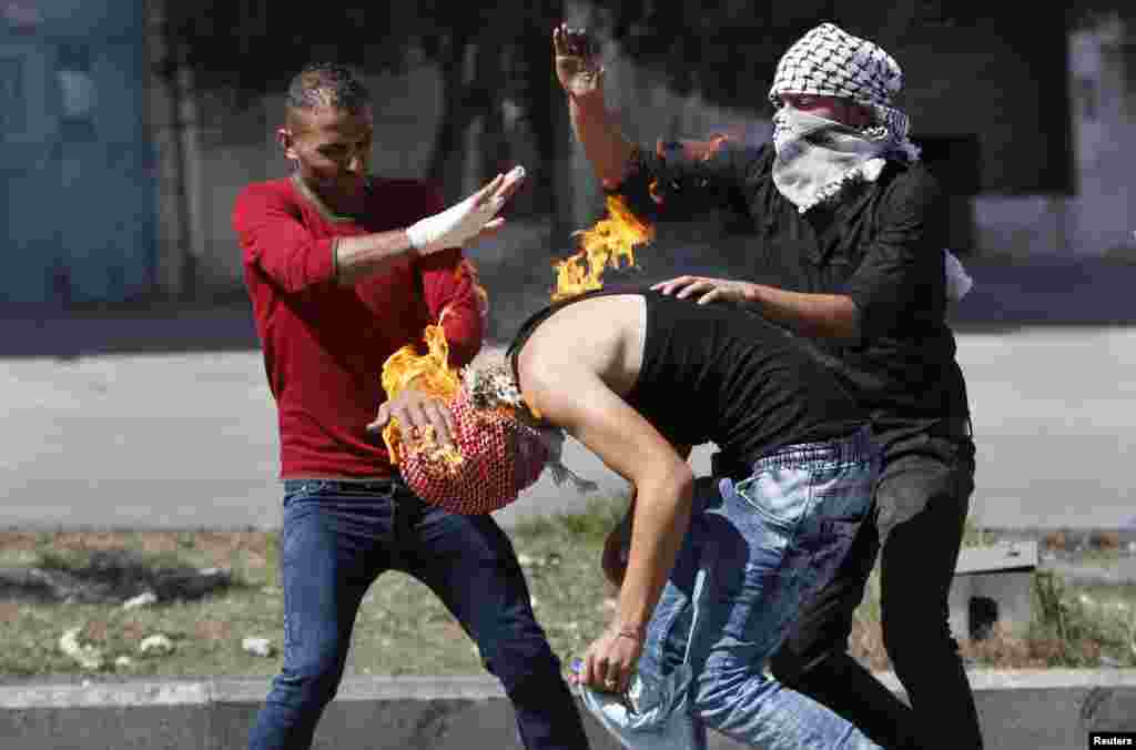 Demonstran Palestina memadamkan api yang membakar tubuh rekannya akibat bom molotov yang tadinya akan dilemparkan ke arah tentara Israel dalam bentrokan di kota Tepi Barat, Hebron. Tujuh warga Israel dan 27 warga Palestina, termasuk sembilan orang yang diduga sebagai penyerang dan delapan anak, tewas dalam serangan yang berlangsung di jalan selama hampir dua minggu ini.