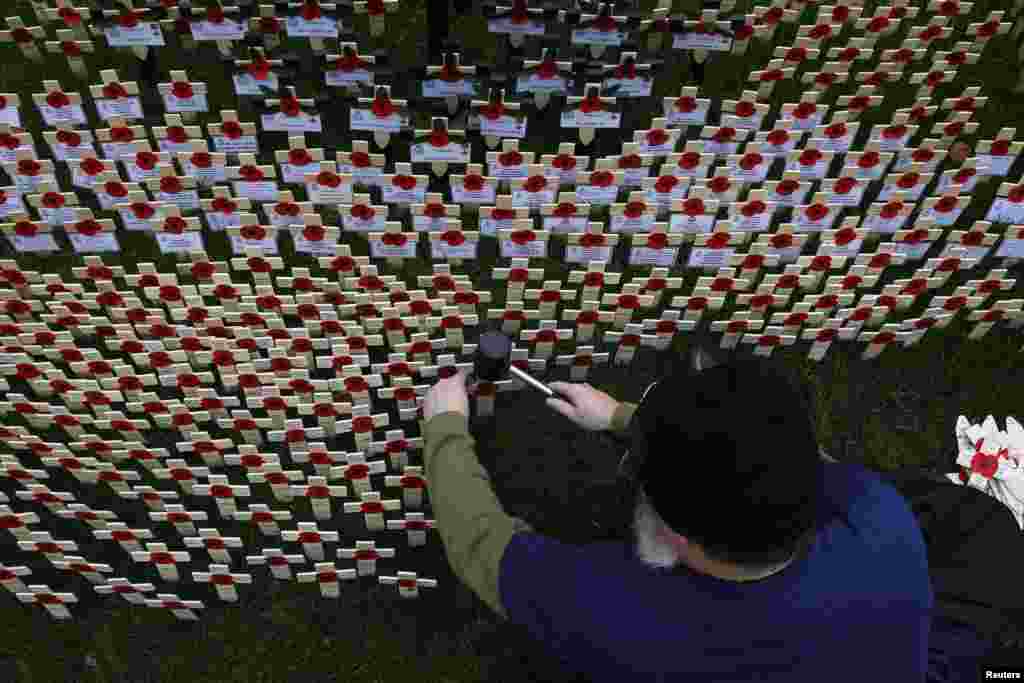 Seorang relawan memasang salib-salib berhiaskan bunga poppy di taman diluar gereja Westminster Abbey, London tengah, Inggris.