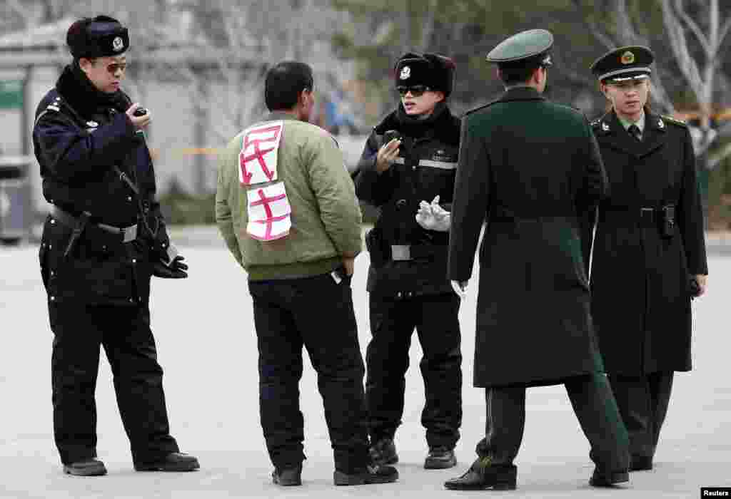 A man with a sign on his back, which reads &#39;democracy&#39;, is questioned by police near the Great Hall of People in Tiananmen Square, central Beijing, China.
