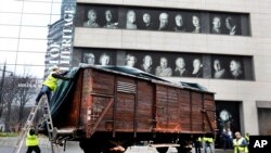 Portraits of Holocaust survivors are displayed at the Museum of Jewish Heritage as a vintage German train car, like those used to transport people to Auschwitz and other death camps, is uncovered on tracks outside the museum, in New York, Sunday, March 31, 2019. 