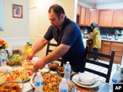 FILE - Syrian refugee Majed Abdalraheem, 29, sets the table at his home in Riverdale, Md., as he and his wife, Walaa Jadallah, prepare for the iftar meal during Ramadan, May 25, 2018.