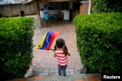 FILE - A girl waves the Venezuelan flag during a visit to bid goodbye in her grandparents' house, before her move to the U.S. after winning the green card lottery, in Valencia, April 6, 2014.