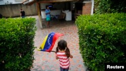FILE - A girl waves the Venezuelan flag during a visit to bid goodbye in her grandparents' house, before her move to the U.S. after winning the green card lottery, in Valencia, April 6, 2014. 