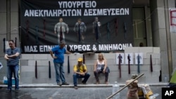 Protesting hospital staff sit in front of a wall that they built at the entrance of the Greek Finance Ministry with a banner depicting Greek Prime Minister Alexis Thipras, Deputy Health Minister Pavlos Polakis and Greek Finance Minister Euclid Tsakalotos wearing ties reading ''Ministry of broken promises" and " We drown in debt and bailouts" in central Athens, June 16, 2017.