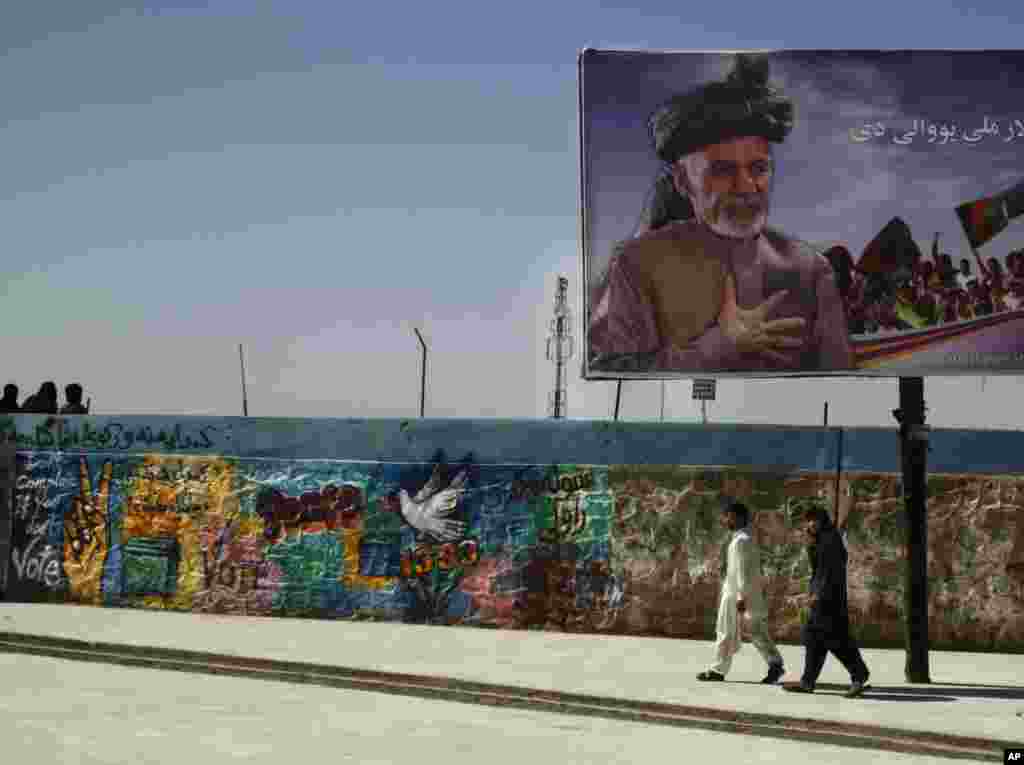 Afghan men pass an election poster showing presidential candidate Ashraf Ghani Ahmadza in the center of Kandahar, March 31, 2014.